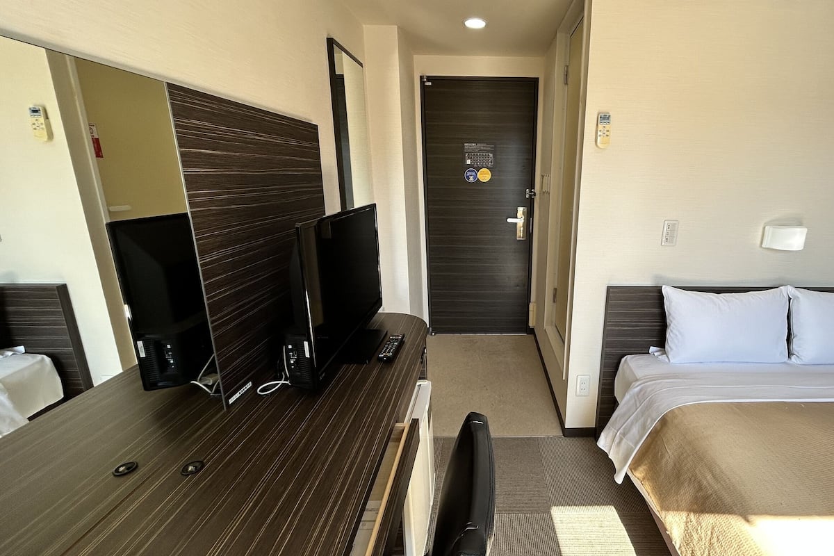 A hotel room with a bed, a desk with a computer, a TV, and a mirror.