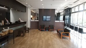 A modern reception area with a wooden floor, a reception desk, and seating. - Smile Hotel Kokura (Kitakyushu)