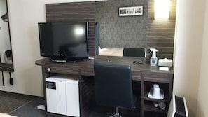 Ein Hotelzimmer mit Bett, Schreibtisch mit Fernseher, Haartrockner und kleinem Kühlschrank.