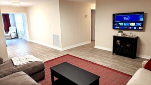 Un salon avec un téléviseur à écran plat fixé au mur, une table basse noire et un tapis rouge.