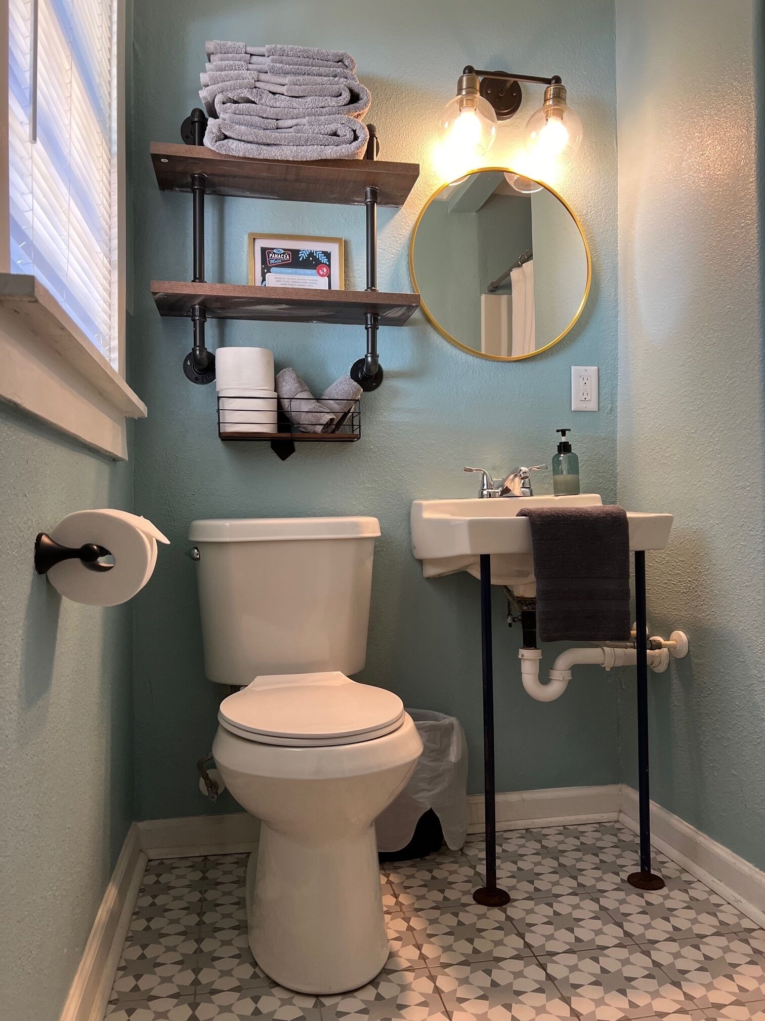 Et badeværelse med toilet, håndvask og spejl. Der er håndklæder på en hylde, toiletpapir og en sæbe.