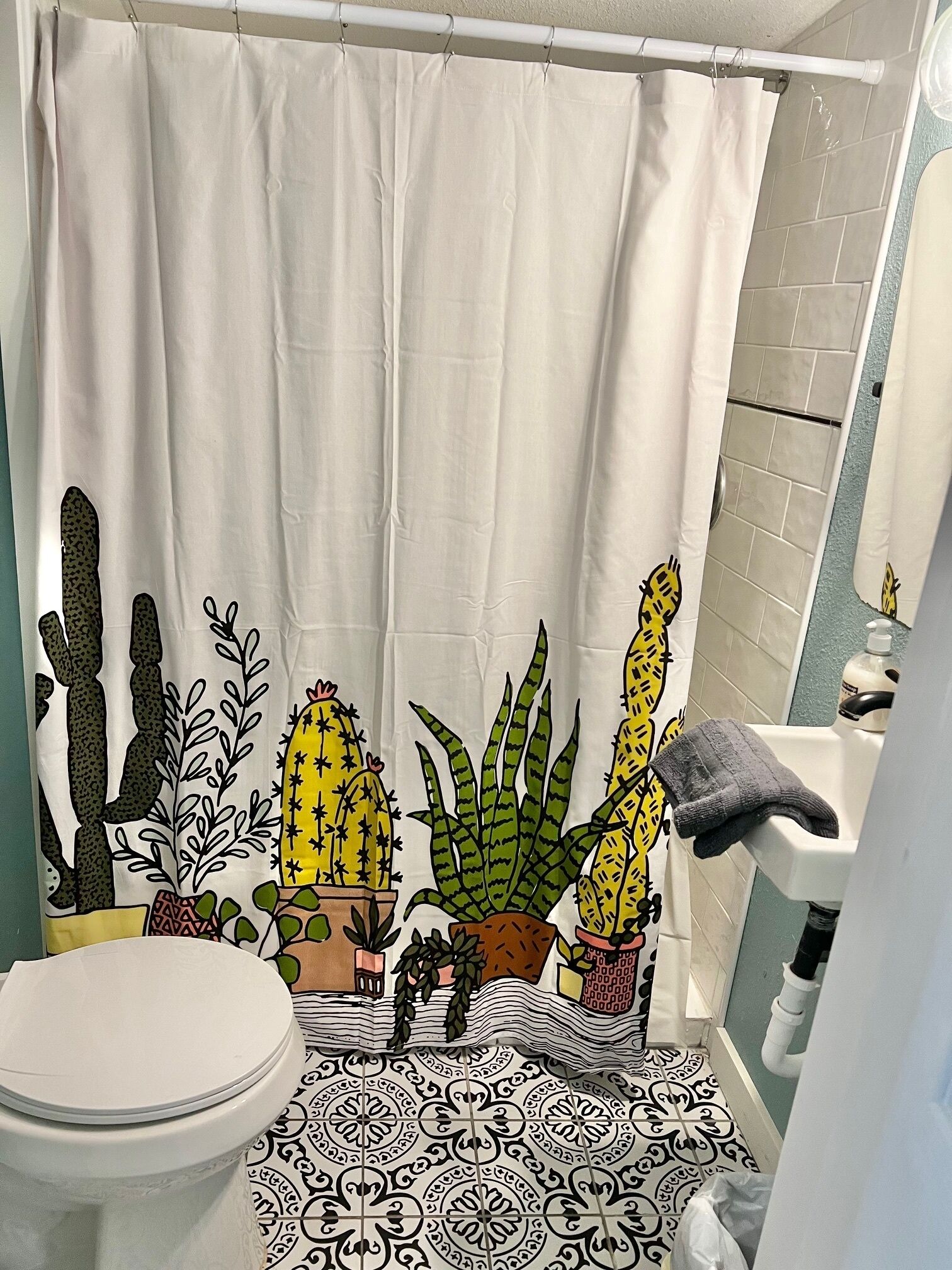 Une salle de bain avec un rideau de douche orné d’un motif de cactus, des toilettes et un lavabo sur lequel est posée une serviette.