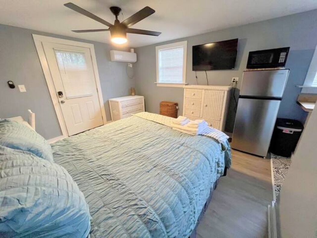 Une chambre à coucher comprenant un lit, un ventilateur de plafond, une télévision, un réfrigérateur et une commode.