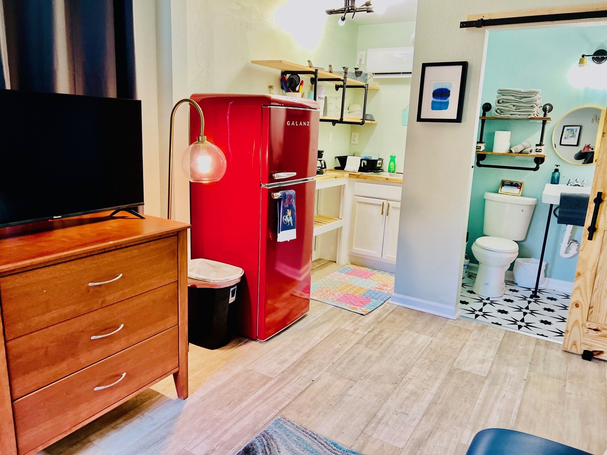 A compact living space with a red refrigerator, a wooden dresser, a television, and a kitchenette.