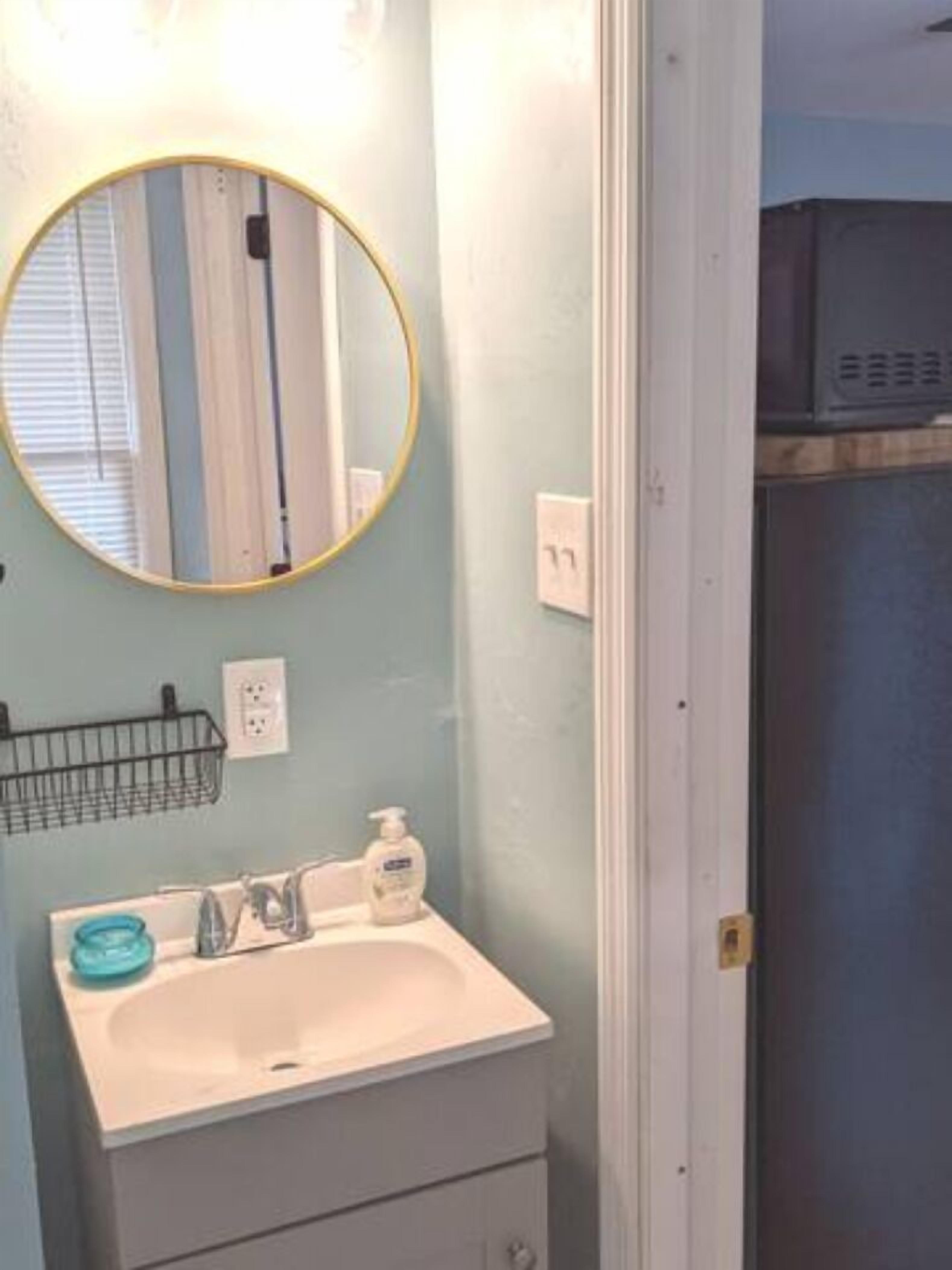 A bathroom with a round mirror, a sink, a soap dispenser, and a towel rack.