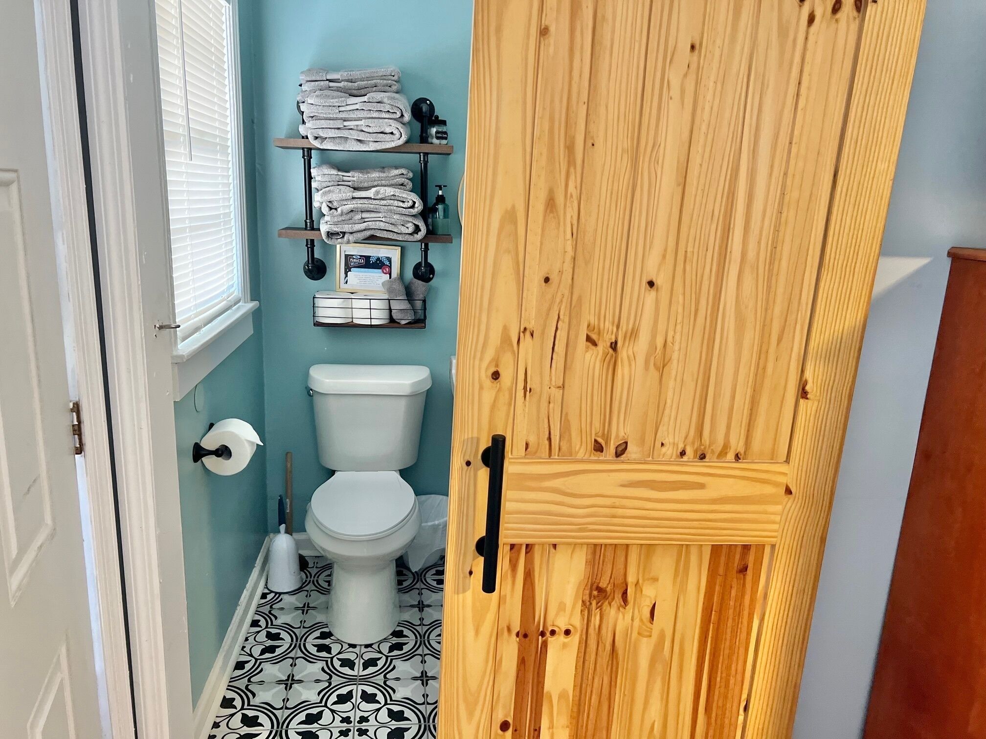 A bathroom with a toilet, a shelf with towels, and a wooden door.