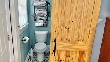 A bathroom with a toilet, a shelf with towels, and a wooden door.
