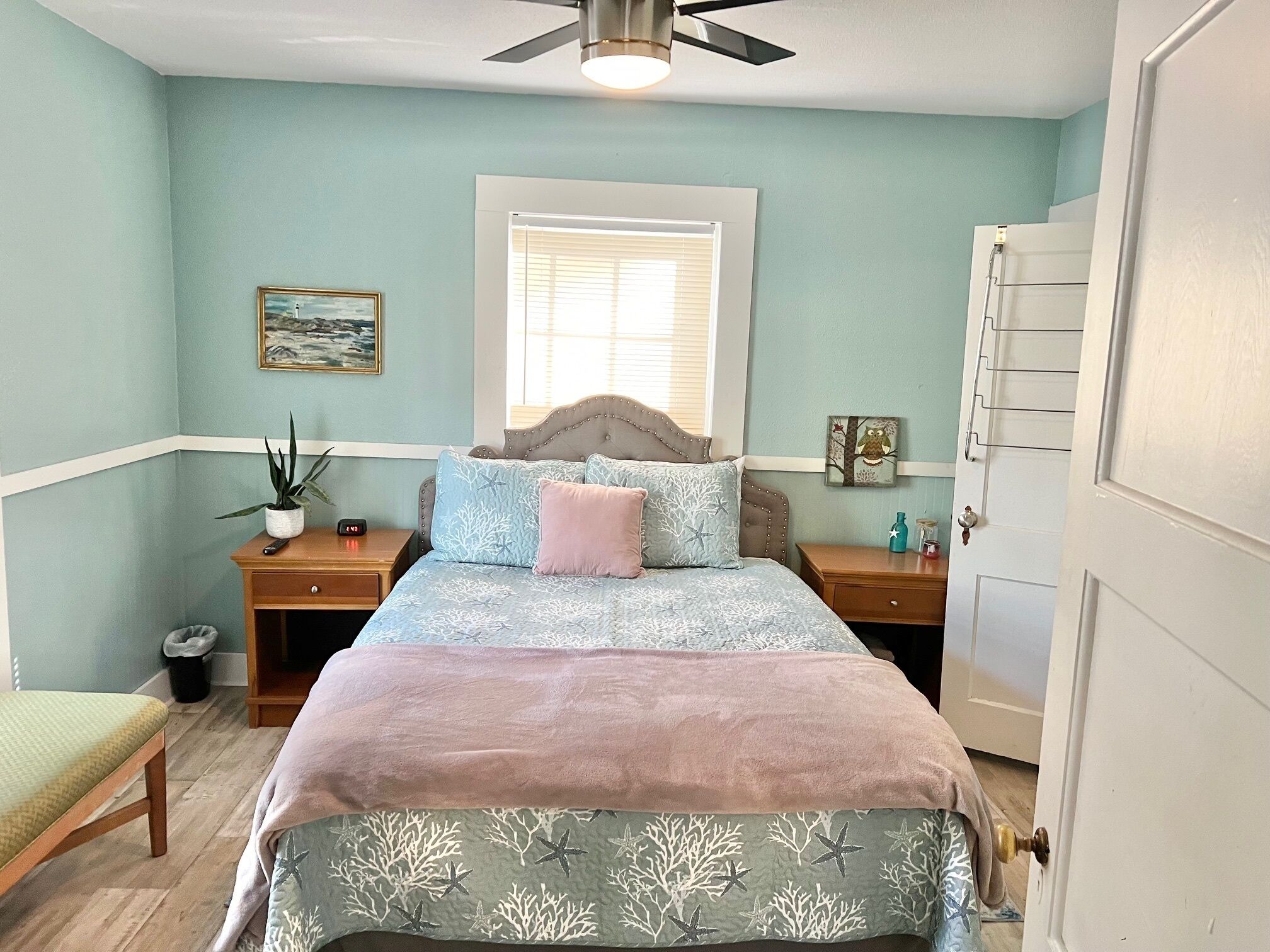 A bedroom with a bed, two nightstands, a window, a ceiling fan, and a door.