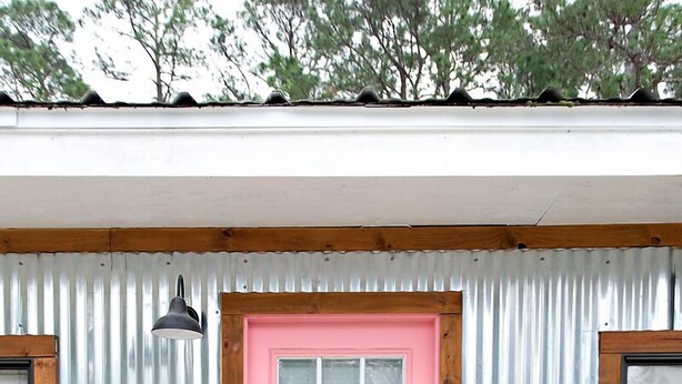 A pink door with a window, set in a corrugated metal exterior with wooden trim.