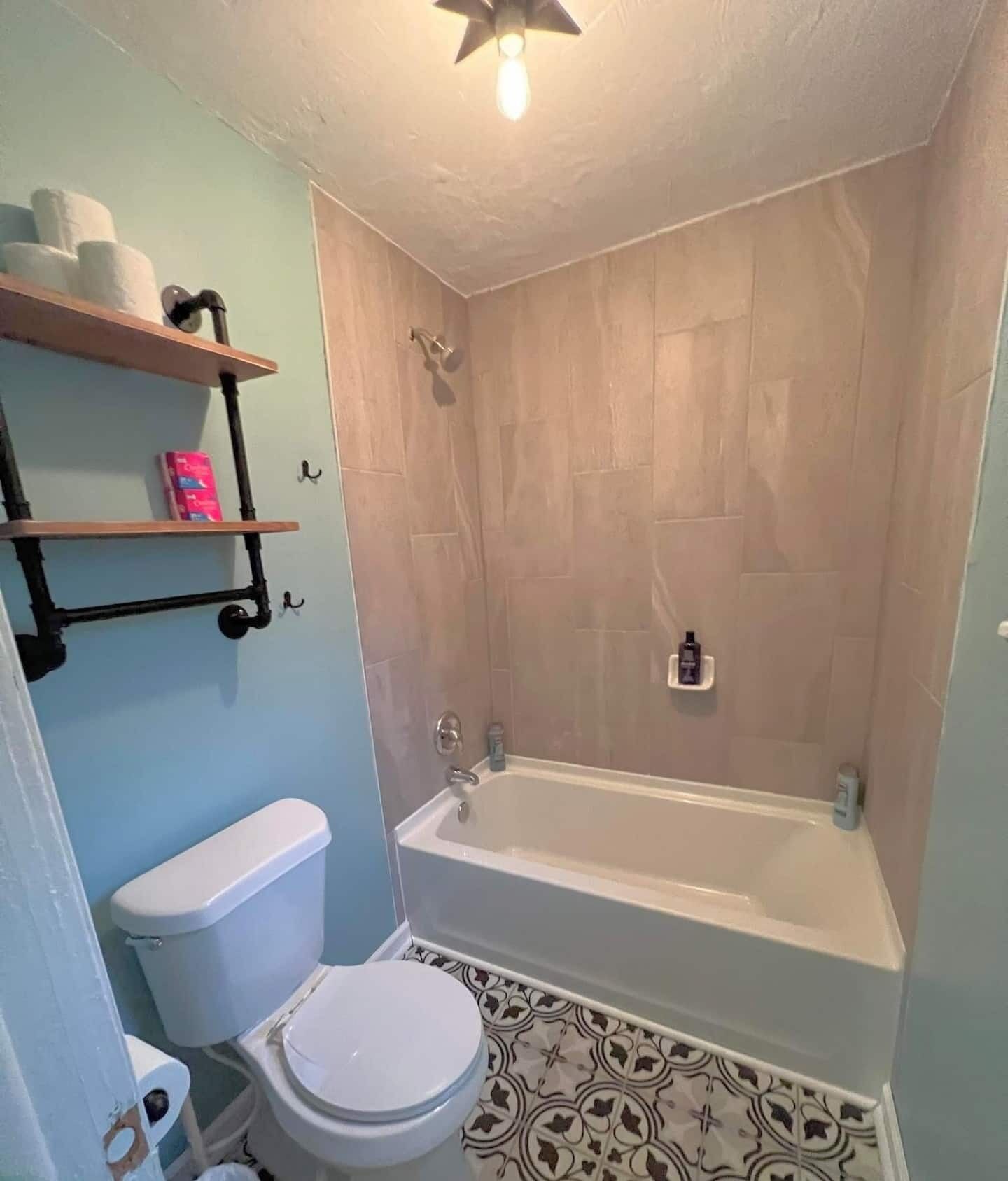 A bathroom with a toilet, a bathtub, and a shower. There are shelves with toiletries and a bottle on the wall.