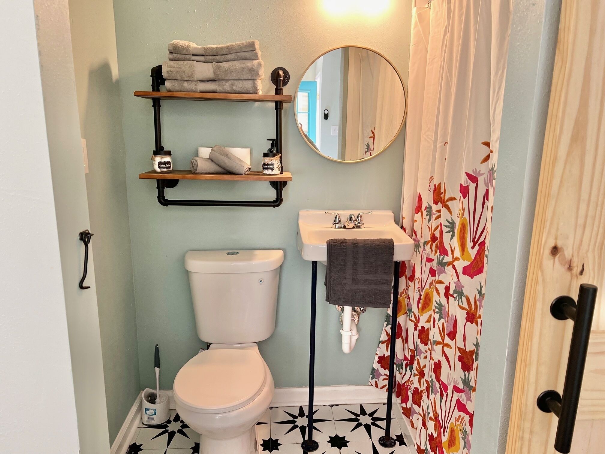 A bathroom with a toilet, a sink, a mirror, and a shelf with towels and toiletries.