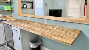 A kitchen with a wooden countertop, a built-in sink, and a trash can.