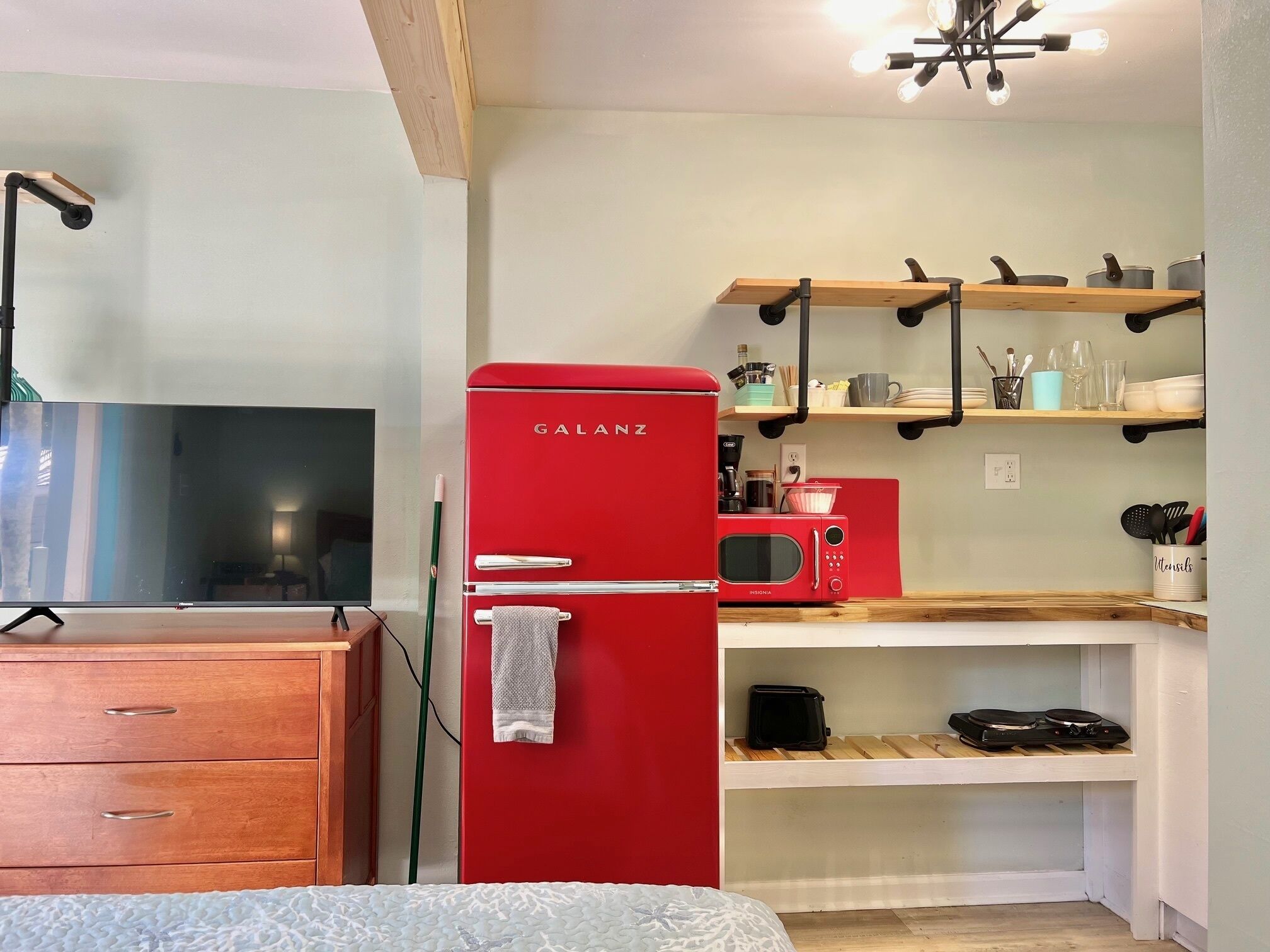 A compact kitchen with a red Galanz refrigerator, a microwave, and wooden shelves above.