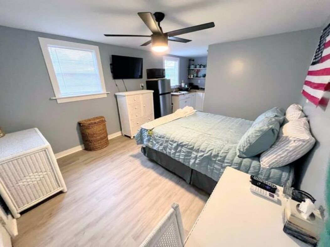 A bedroom with a bed, a ceiling fan, a radiator, a small table, and a TV.