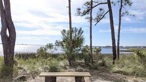A wooden bench in a natural setting with trees and a body of water in the background.