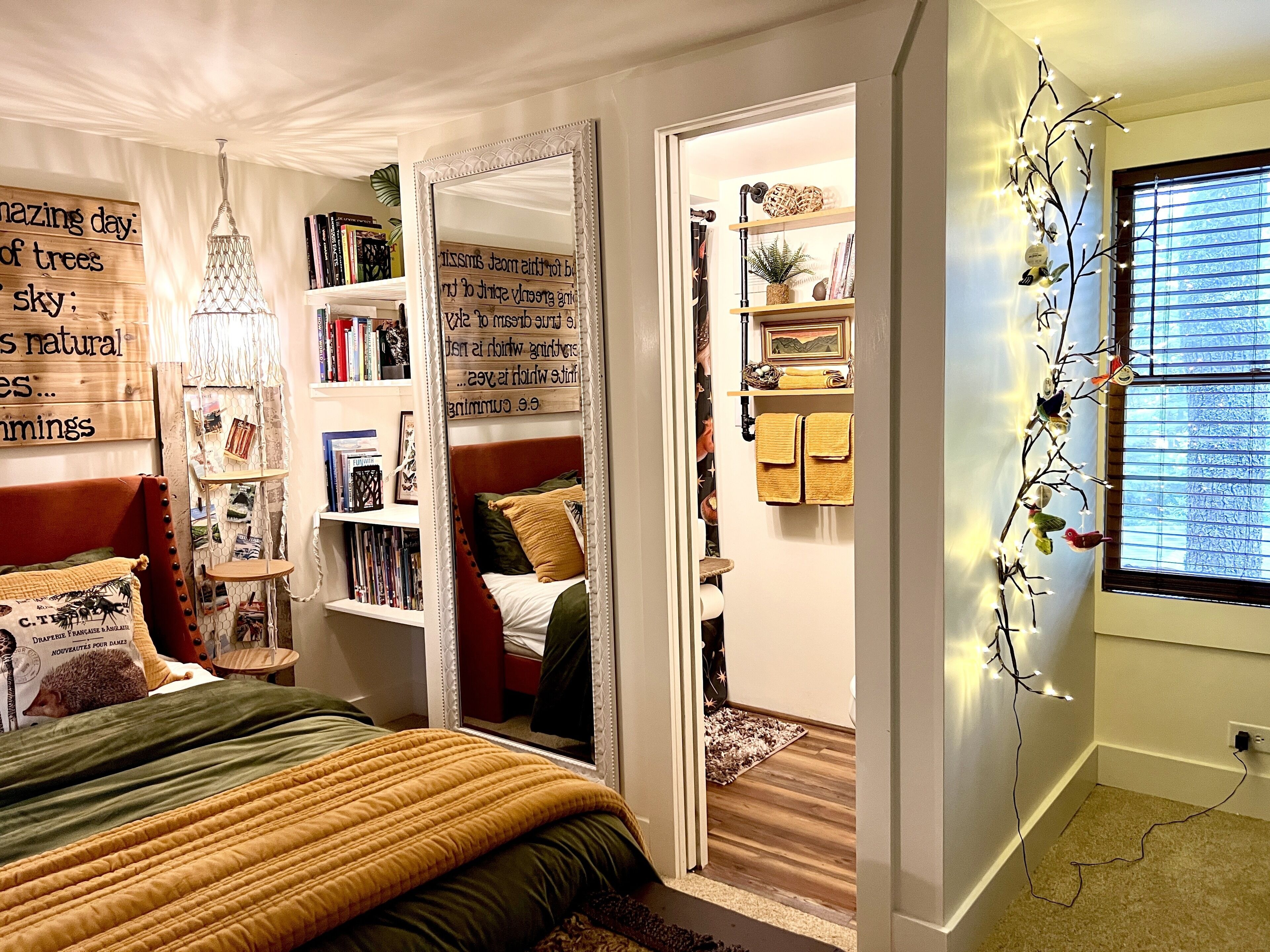 Ein Schlafzimmer mit Bett, Bücherregal, Spiegel und Fenster mit Jalousien.