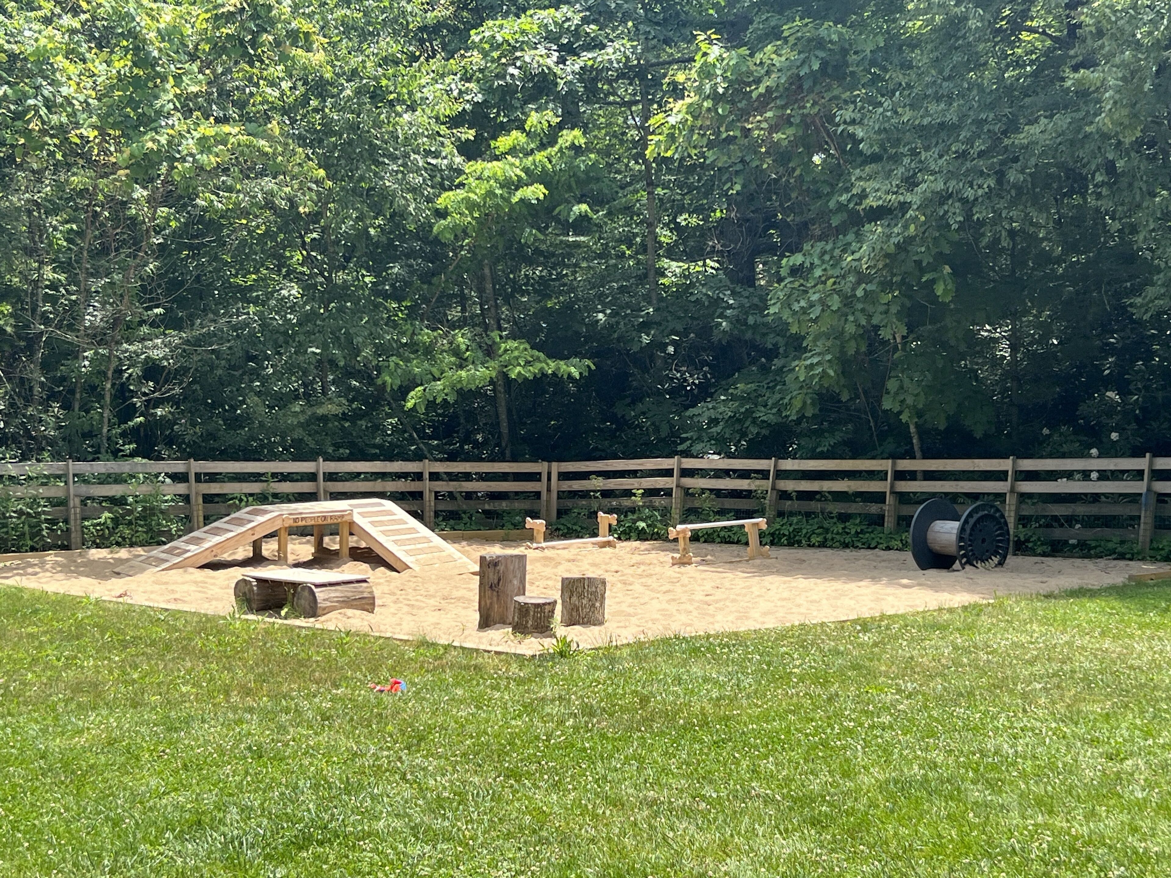 A fenced outdoor area with a sandy play area, wooden benches, and a large log.