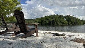 Een strandstoel op een zandstrand, met een meer en bos op de achtergrond.