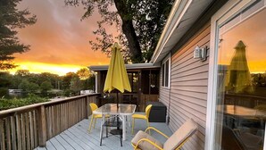 Eine Terrasse mit Tisch, Stühlen, einem gelben Sonnenschirm und einem Schaukelstuhl.