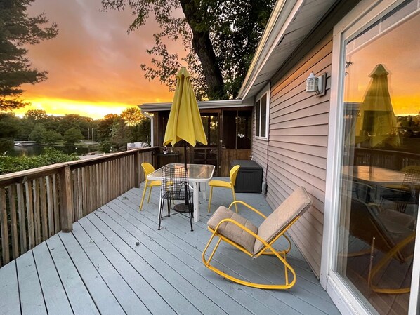A deck with a table and chairs, a yellow umbrella, and a rocking chair. - Cozy Hudson Valley Lake Cottage :4 Kayaks + a Canoe, 400 acre Lake (Craryville)