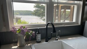 Eine Küche mit einem weißen Spülbecken, einem schwarzen Wasserhahn und einem Fenster mit Blick auf ein Gewässer.