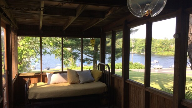 Eine Holzterrasse mit einem Bett, großen Fenstern und Seeblick.