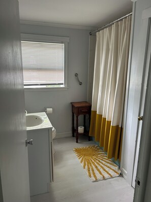 A bathroom with a sink, window with blinds, shower curtain, and a small wooden side table. - Cozy Hudson Valley Lake Cottage :4 Kayaks + a Canoe, 400 acre Lake (Craryville)