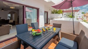 A dining area with a table set for two, surrounded by wicker chairs, a large umbrella, and a view of the cityscape. - Casa Maestranza (Marbella)