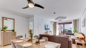 A modern living room with a dining area, featuring a wooden table set for a meal, a sofa, and a television mounted on the wall. - Casa Maestranza (Marbella)