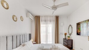 A modern hotel room with a large bed, a ceiling fan, a flat-screen TV, and a view of the city through the window. - Casa Maestranza (Marbella)