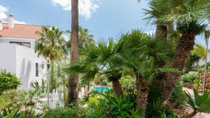 A lush garden with palm trees, a variety of plants, and a pool in the background. - Casa Maestranza (Marbella)