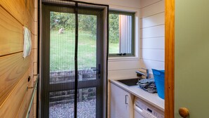 A compact laundry room with a washing machine, a sink, and a window. - Moa Cottage in Oneroa Village (Waiheke Island)