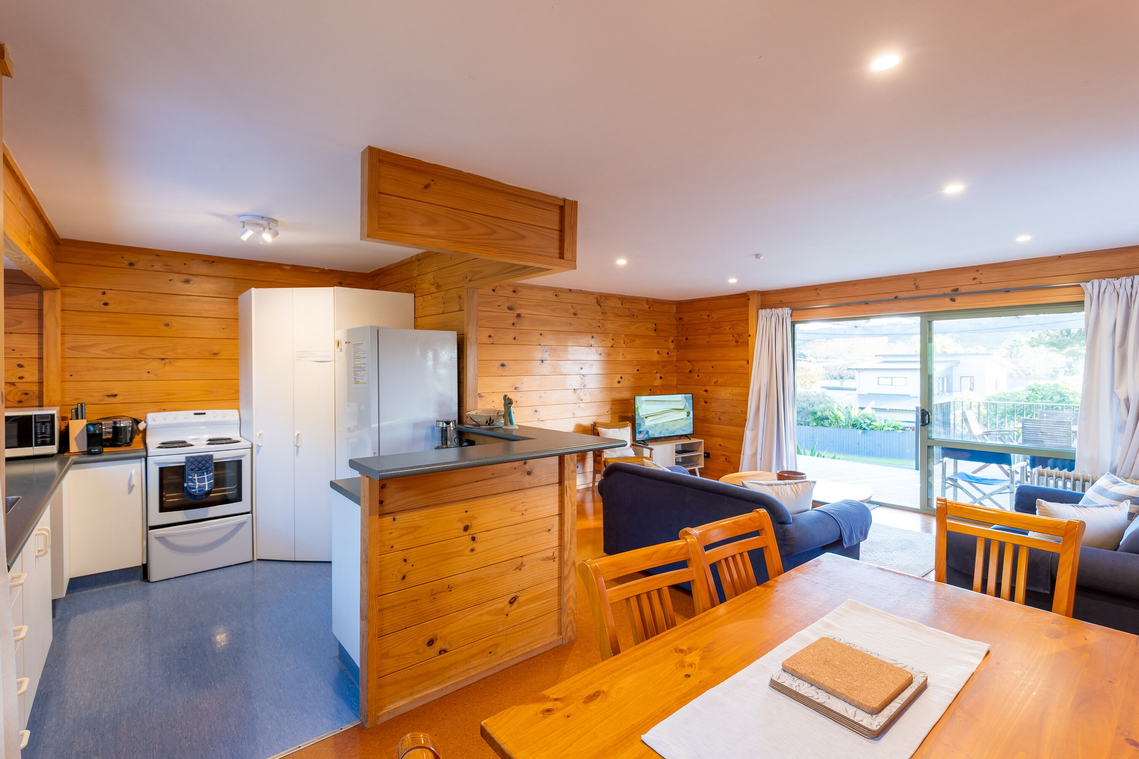 A compact kitchen with a stove, microwave, and refrigerator. There is a dining table with chairs and a sofa in the adjacent living area.