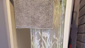 A shower area with a beige textured mat, a floral shower curtain, and a red broom leaning against the wall. - On the waters edge of Lake Cecebe Tranquility above Muskoka at Rockwynn Cottages (Burk's Falls)