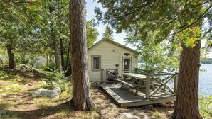 A cabin with a deck and a dock, surrounded by trees and a lake. - On the waters edge of Lake Cecebe Tranquility above Muskoka at Rockwynn Cottages (Burk's Falls)