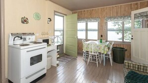 A cozy kitchen with a stove, microwave, and coffee maker, a dining table with chairs, and large windows overlooking a body of water. - On the waters edge of Lake Cecebe Tranquility above Muskoka at Rockwynn Cottages (Burk's Falls)