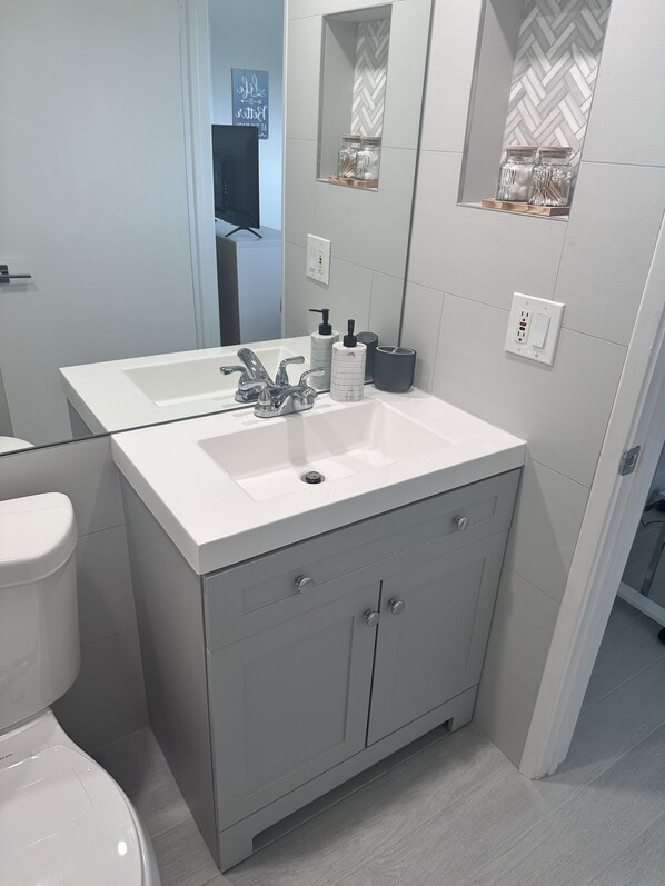 A modern bathroom with a white sink, two faucets, a mirror, and a toilet. - Jupiter Dreams at Jupiter Bay! 2 bedroom, 2.5 bath Condo. Close to the beach! (Jupiter)