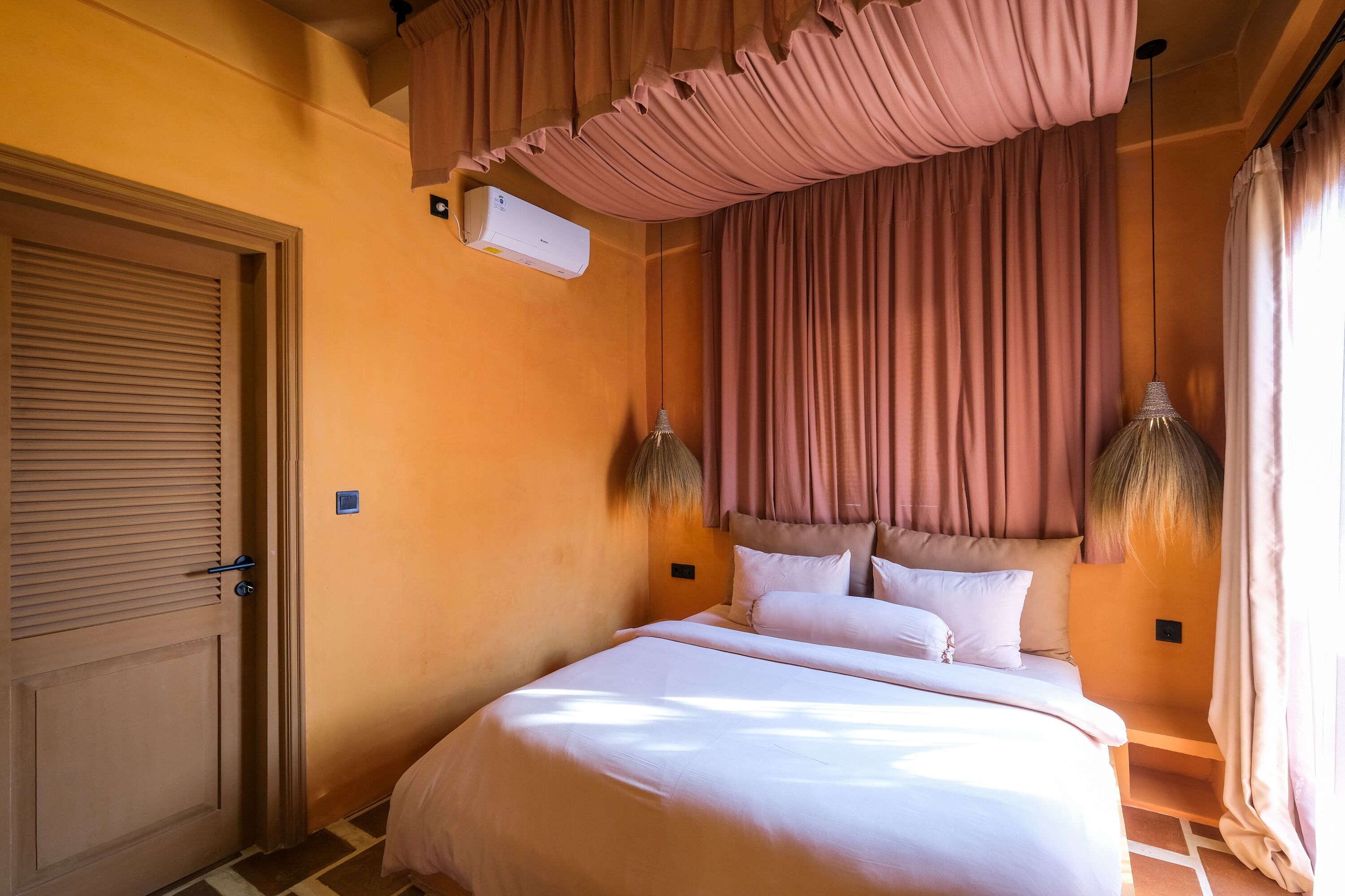 A hotel room with a bed, curtains, an air conditioning unit, and a door.
