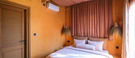 A hotel room with a bed, curtains, an air conditioning unit, and a door.