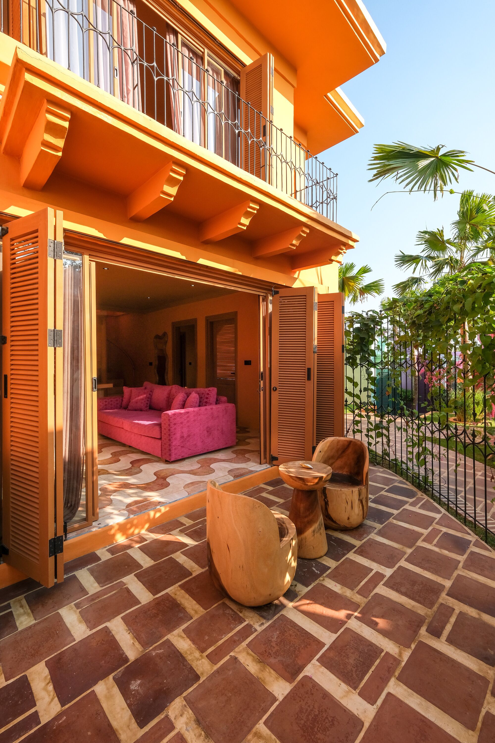 Un bâtiment à deux étages doté d’un balcon, d’un canapé rose et d’une table en bois sur la terrasse.
