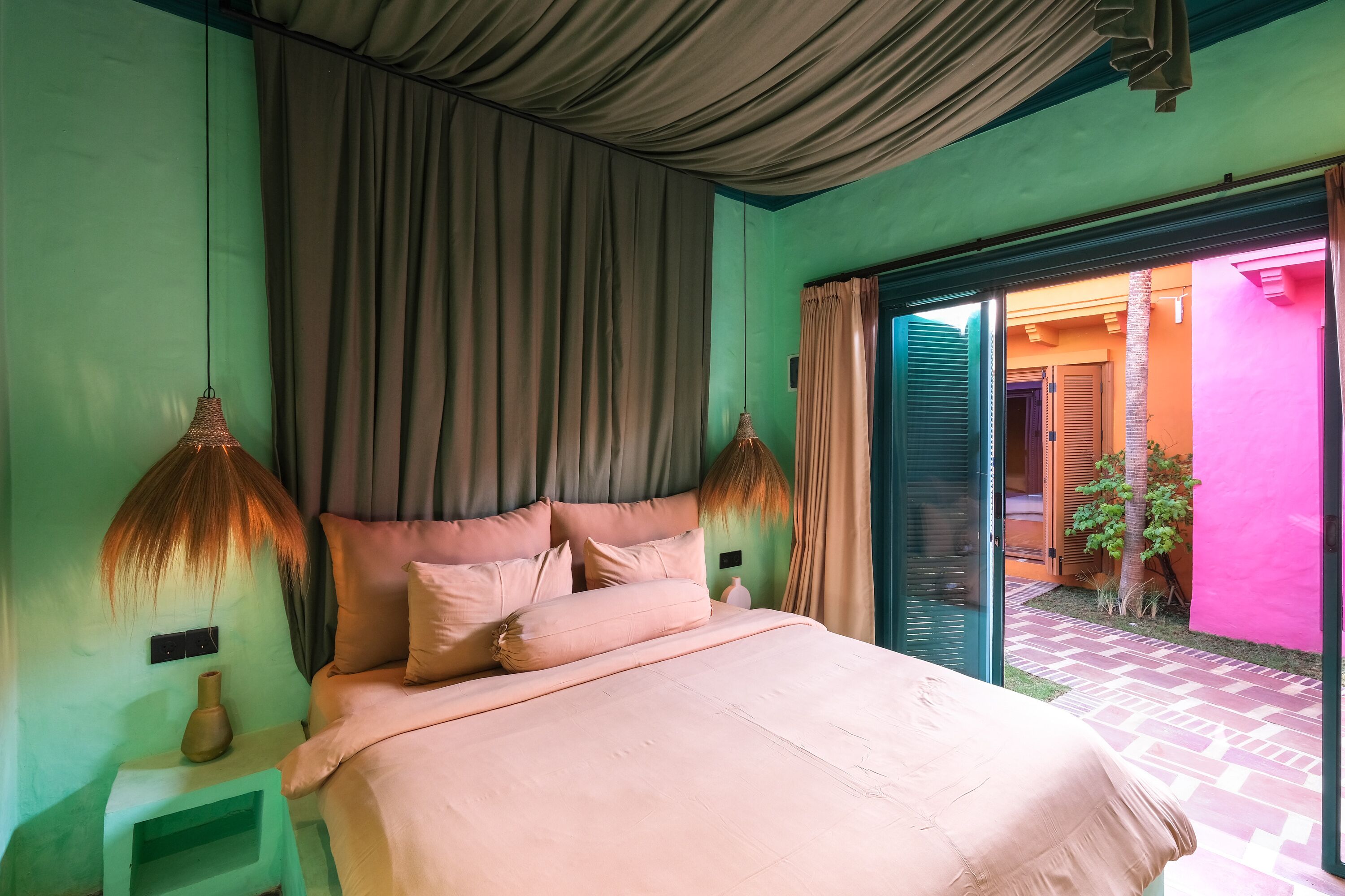 A bedroom with a bed, curtains, a nightstand, and a view of the outside.