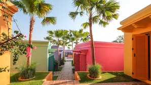 A pathway leading to a building with a red facade, surrounded by palm trees and a small garden area. - El Barrio Boutique Hotel & Bar (Kerobokan)