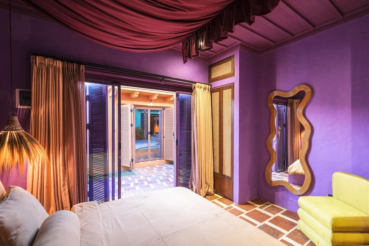 A room with a bed, a yellow armchair, a mirror, and a view through a glass door to an outdoor area.