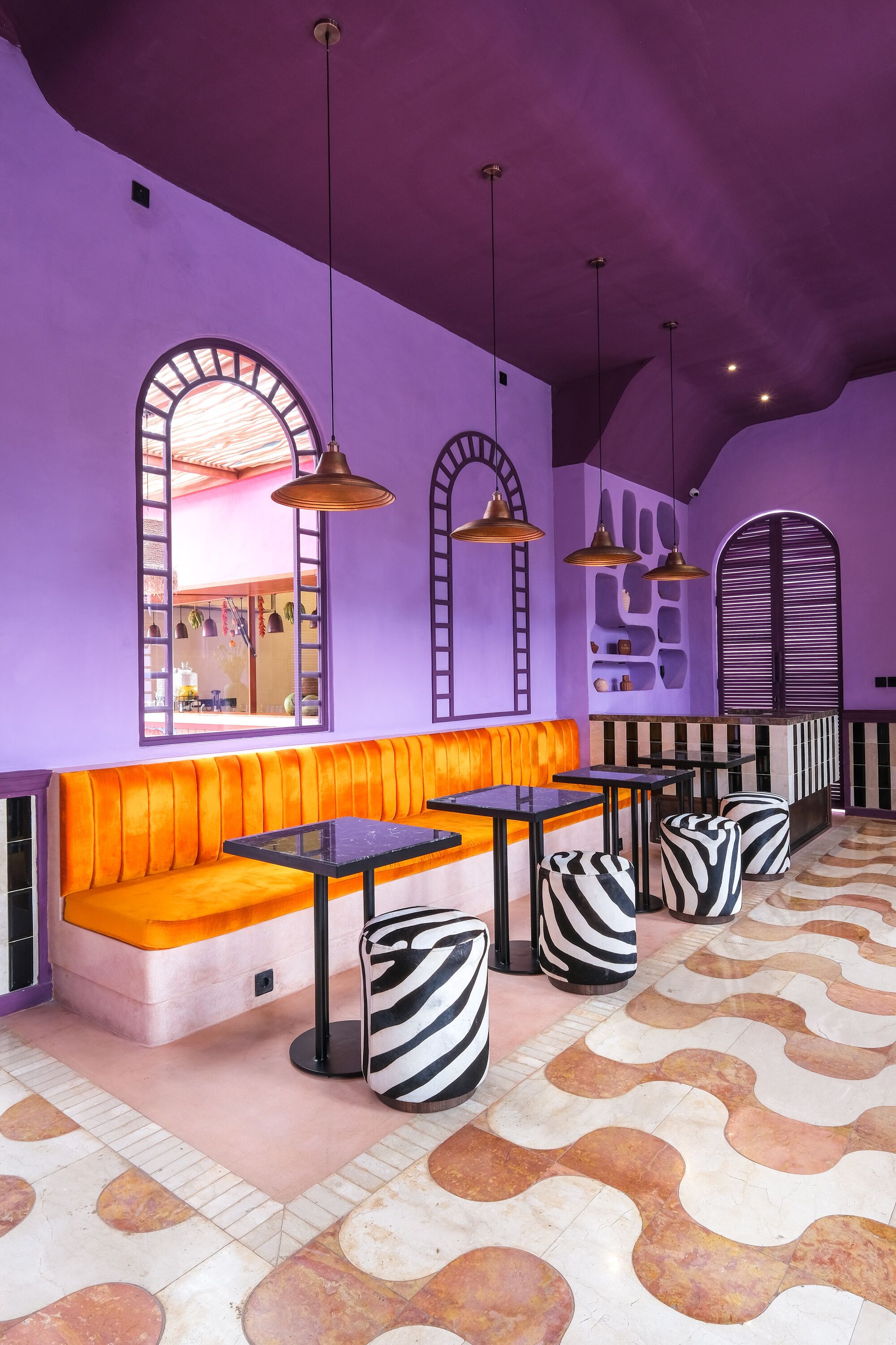 A purple-themed interior with orange seating, black and white patterned ottomans, and pendant lighting.