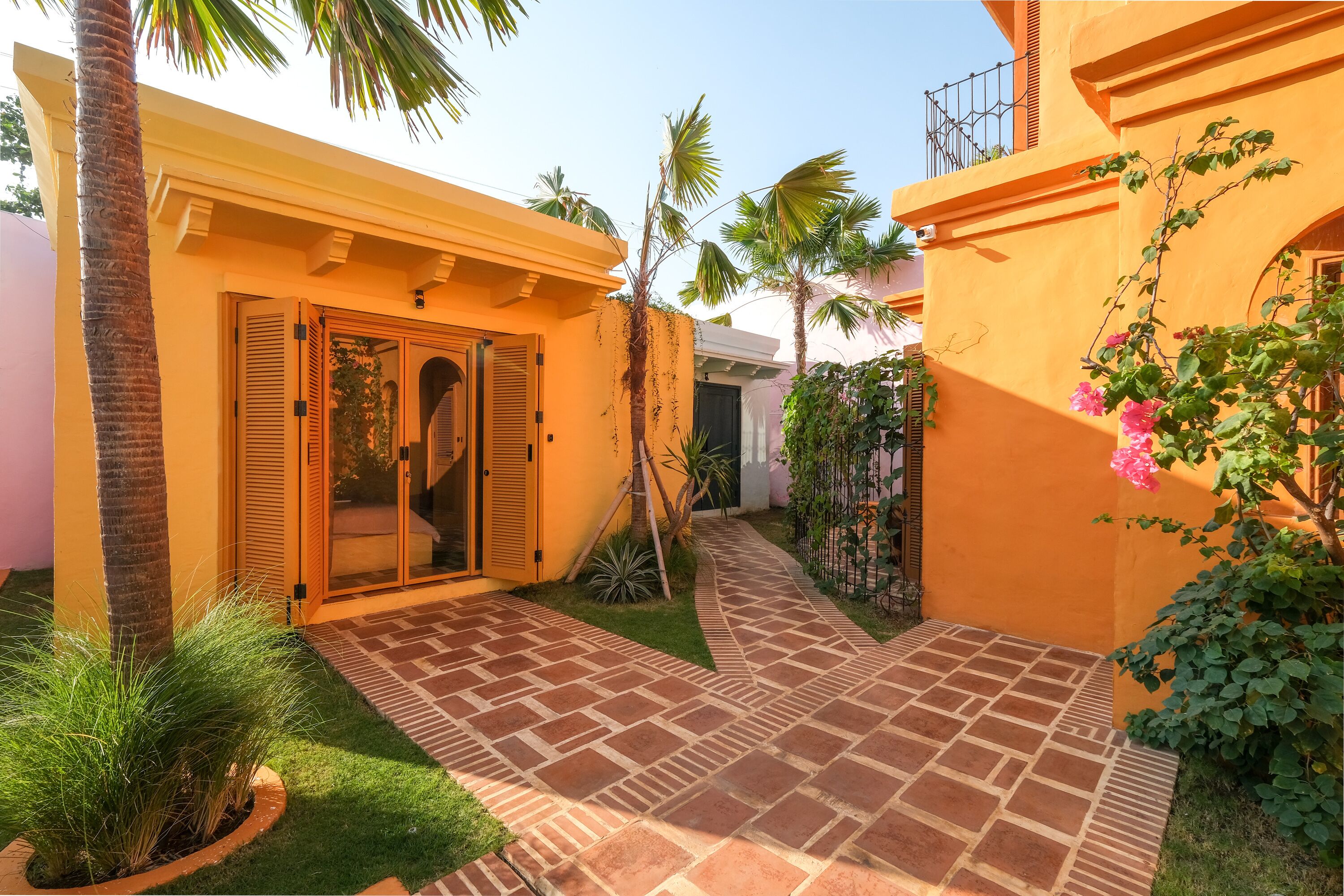 A courtyard with a paved walkway, palm trees, and a building with a yellow facade.