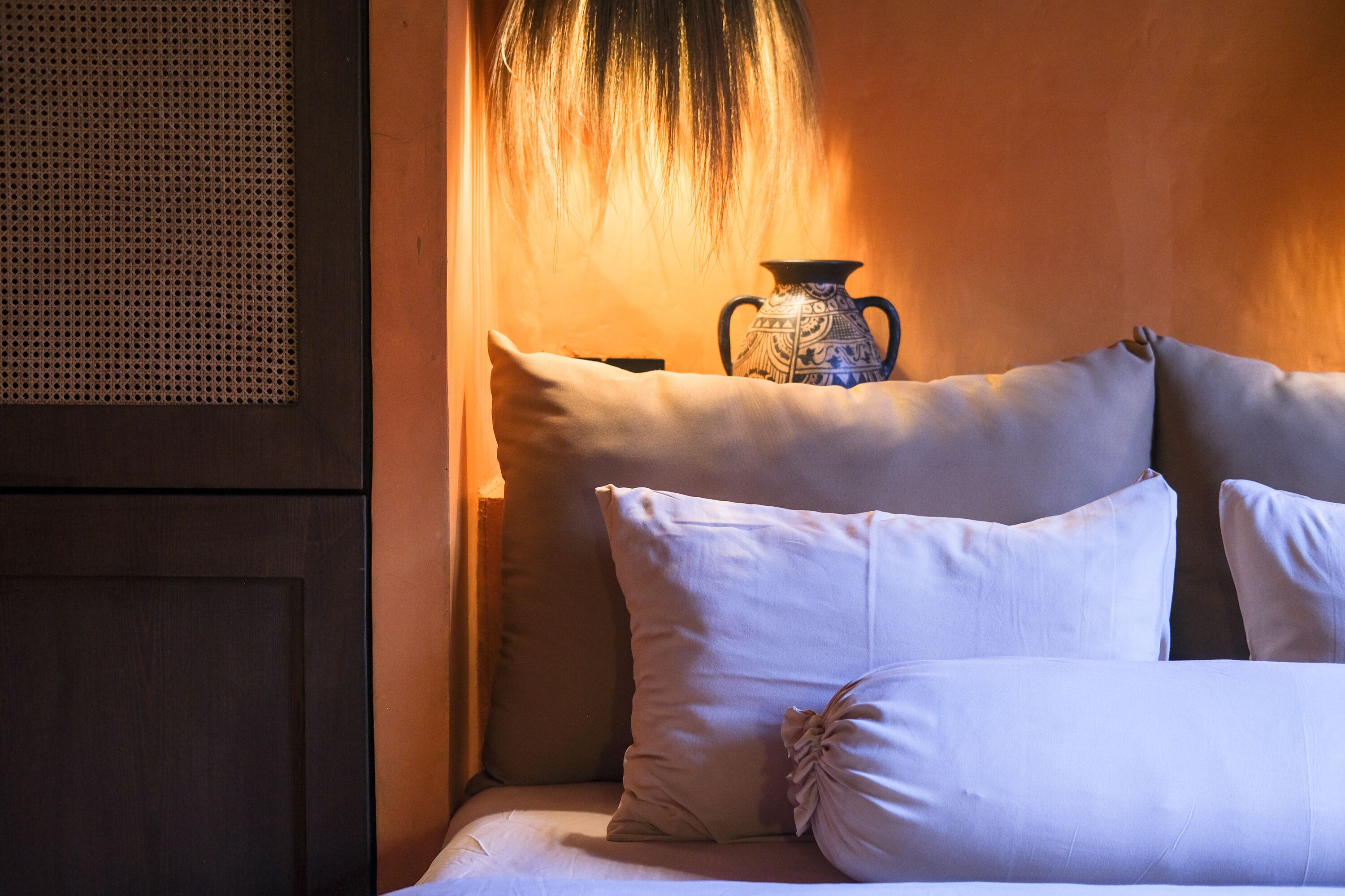 A bed with white pillows and a decorative vase on a wooden nightstand.