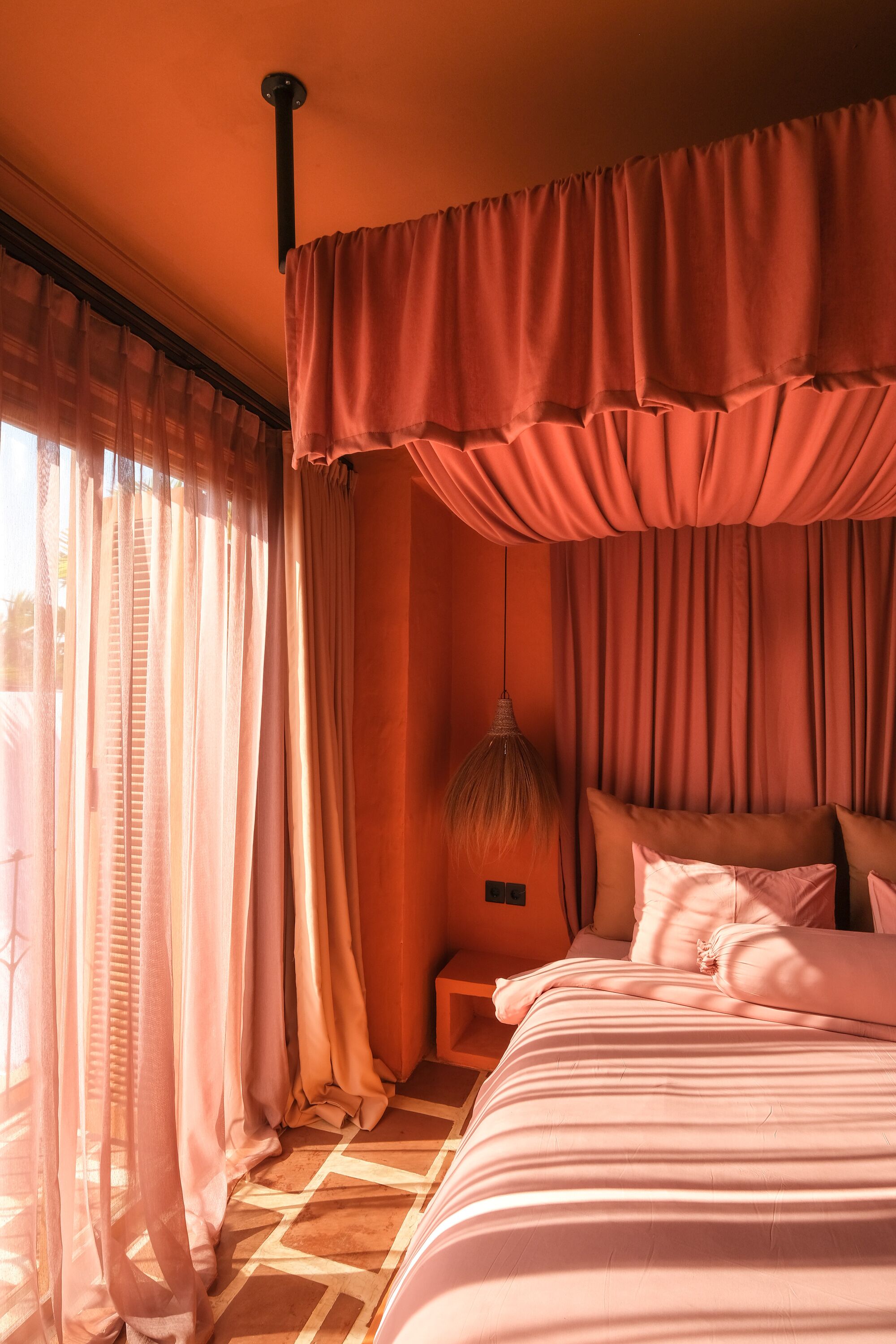 Een slaapkamer met een bed, gordijnen, een lamp en een raam.