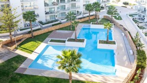 Un hôtel moderne doté d’une piscine centrale, entourée de palmiers et d’une pelouse bien entretenue.