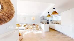 Une cuisine moderne avec des meubles blancs, un coin repas doté d’une table ronde et de chaises, et un grand luminaire tressé.