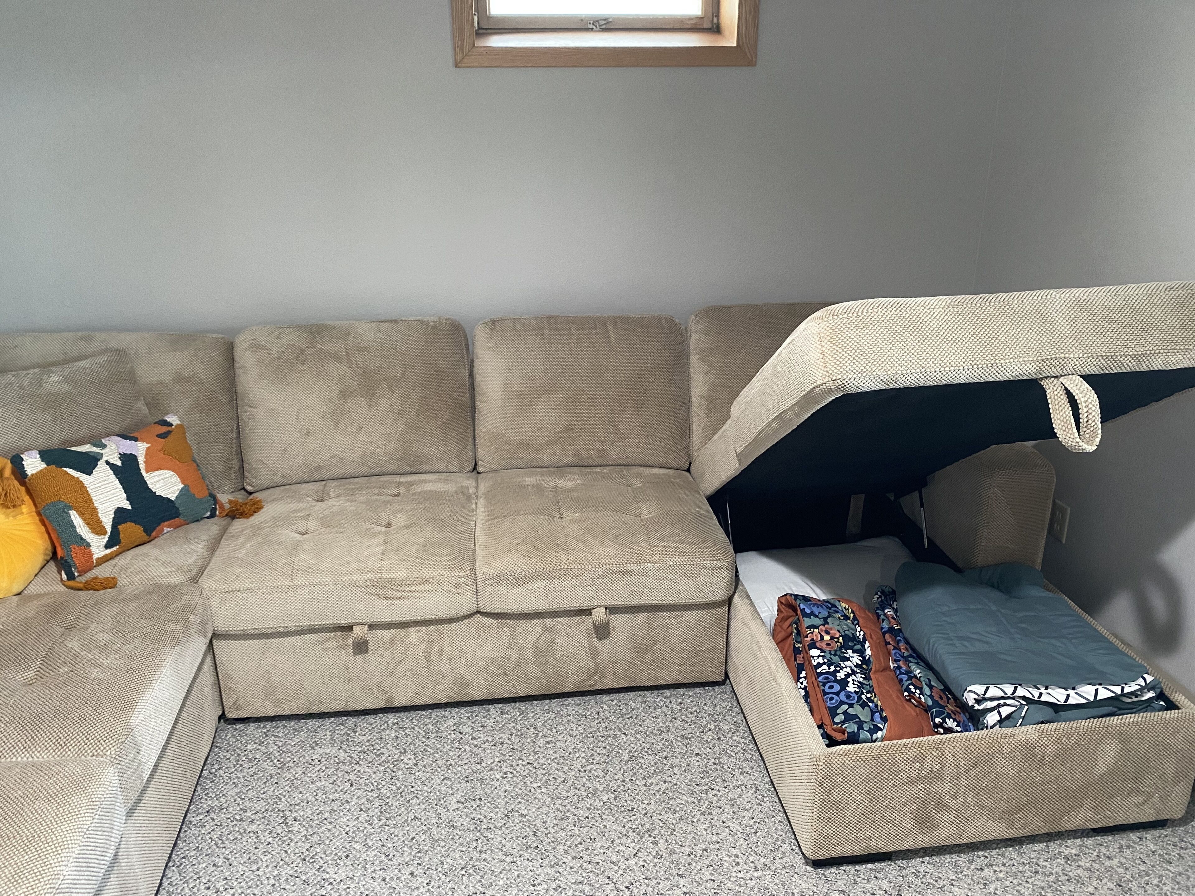 Ein modulares Sofa mit integriertem Stauraumbench, einem kleinen Fenster und einem dekorativen Kissen.